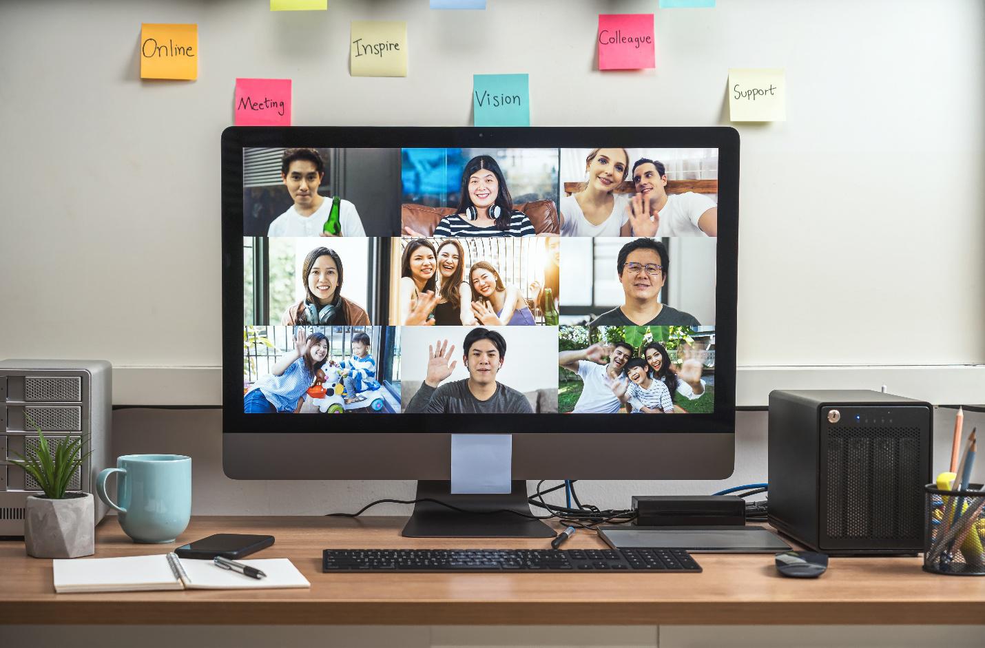 Modern office desk setup featuring a PC monitor displaying a Zoom call, alongside a mobile phone, a small plant, and a coffee cup.