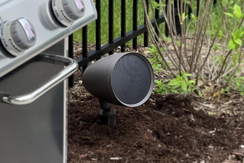A landscape satellite speaker hidden within a garden plant bed for seamless outdoor audio placement.
