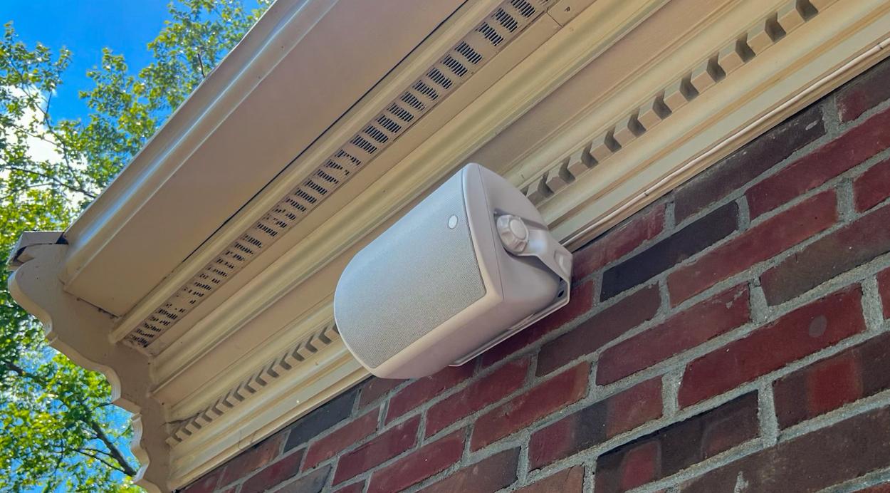 Professional-grade wall-mounted outdoor speaker installed under a roof eave for optimal sound projection on a deck.